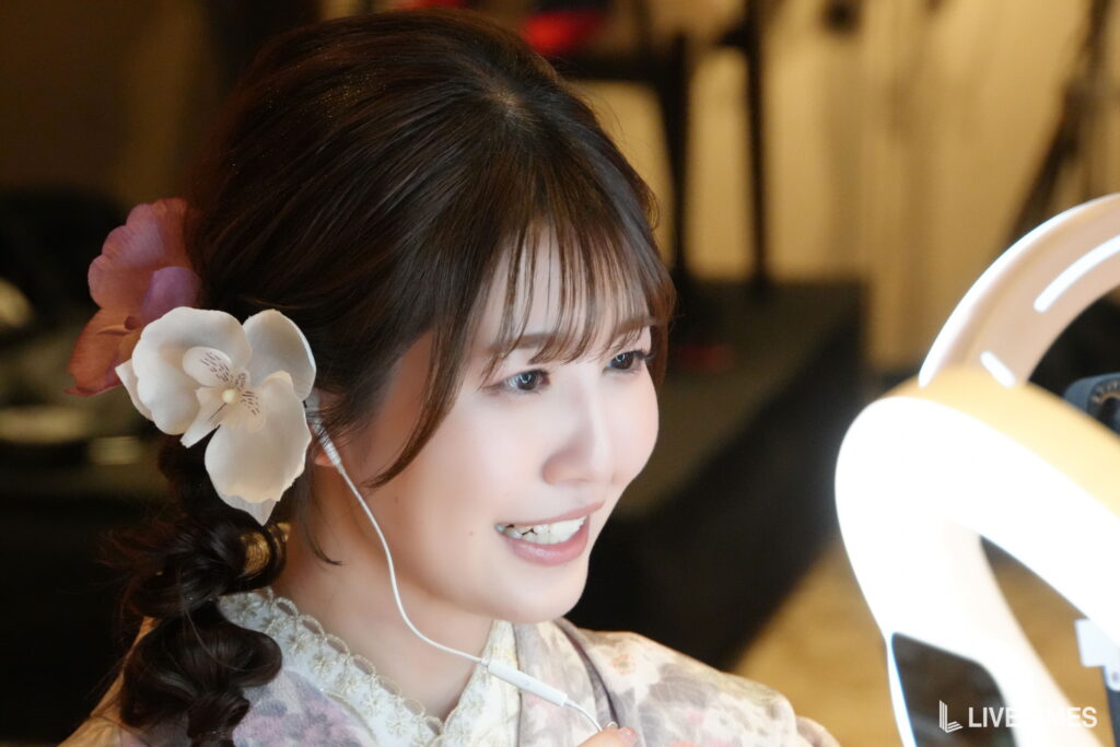 Young woman with a white orchid in her hair, wearing a floral dress and earphones, smiling slightly toward the left.