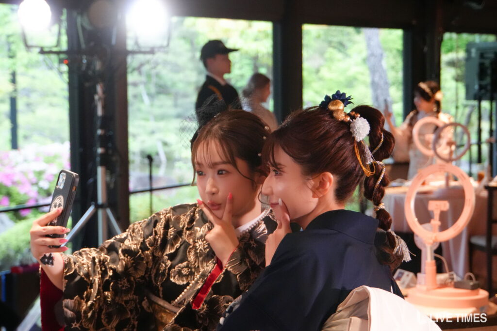 Two women in ornate outfits posing for a selfie, one holding a smartphone.