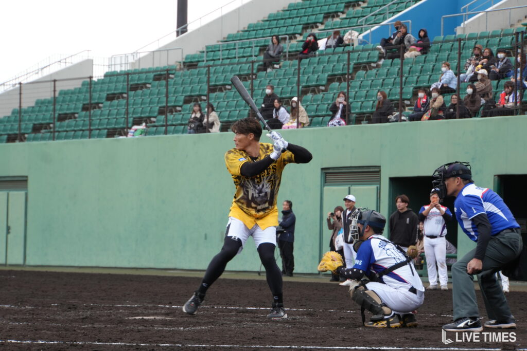 Baseball player in yellow uniform swings at a pitch with catcher and umpire nearby at home plate.