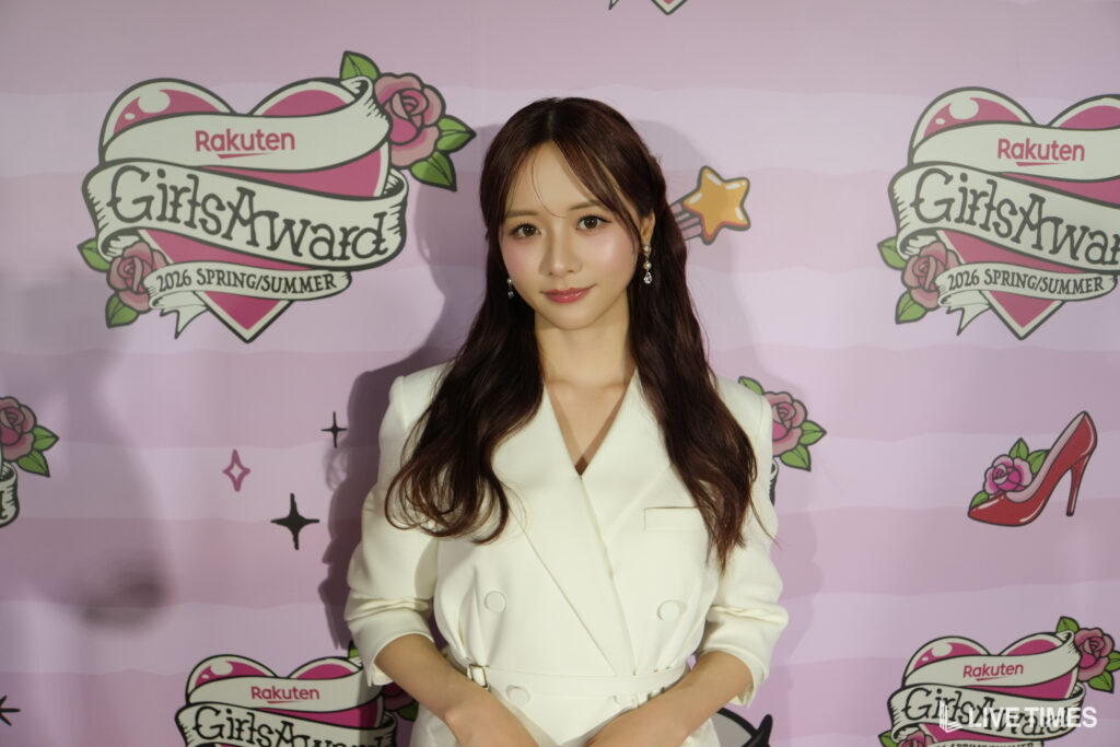 Woman posing at a fashion event in front of a pink backdrop featuring 'GirlsAward' and Rakuten logos.