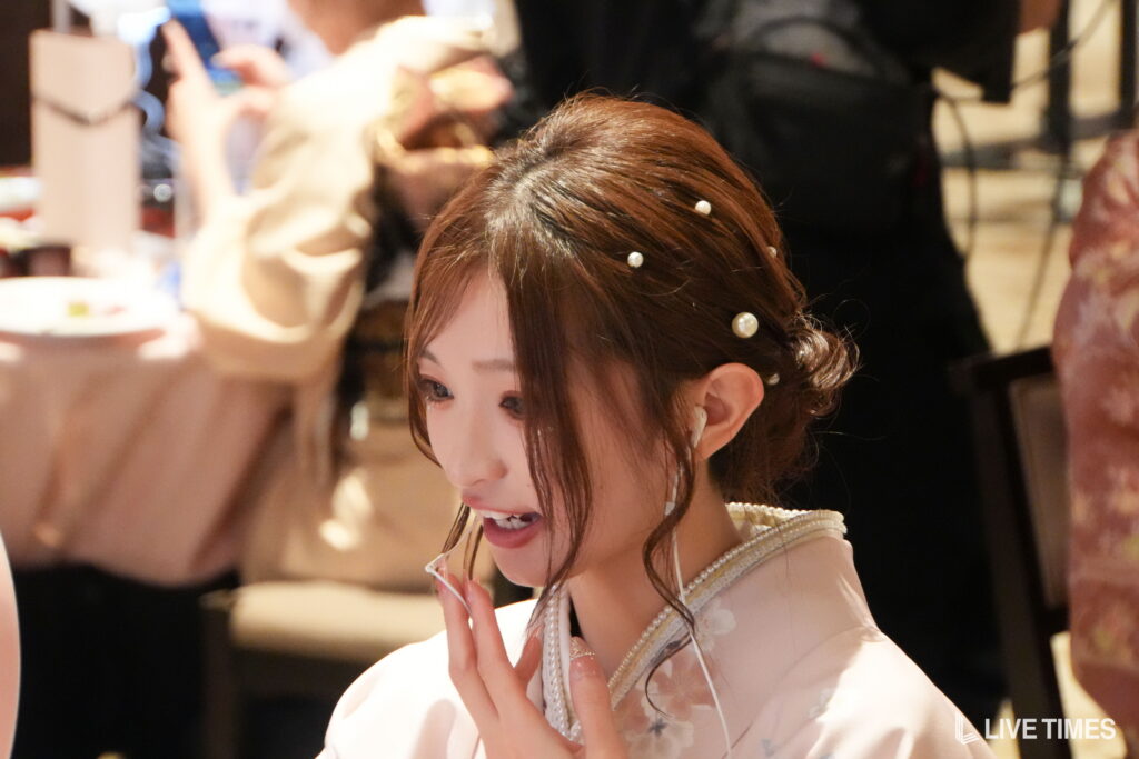 Close-up of a woman at a social event, with pearl hairpins and a pearl necklace, smiling softly.