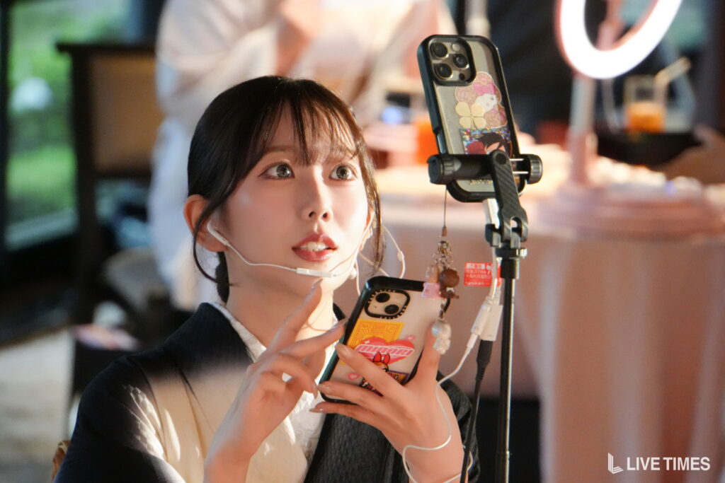Woman recording a video with a smartphone on a tripod, ring light behind, wearing a headset microphone.