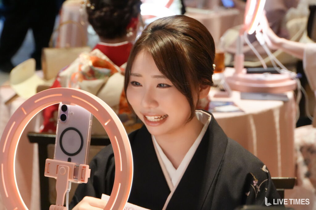 Young woman in a dark kimono smiles while using a pink ring light for a photo setup at an event.