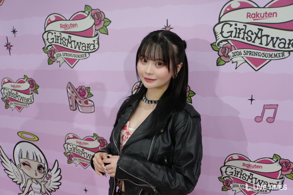 Young woman posing in front of a pink event backdrop with cartoon logos and roses (GirlsAward branding).