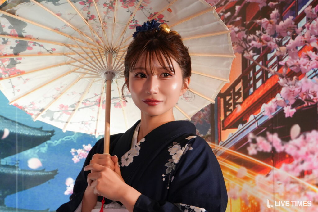 Woman in a dark kimono with floral pattern holding a decorative parasol with cherry blossom design.