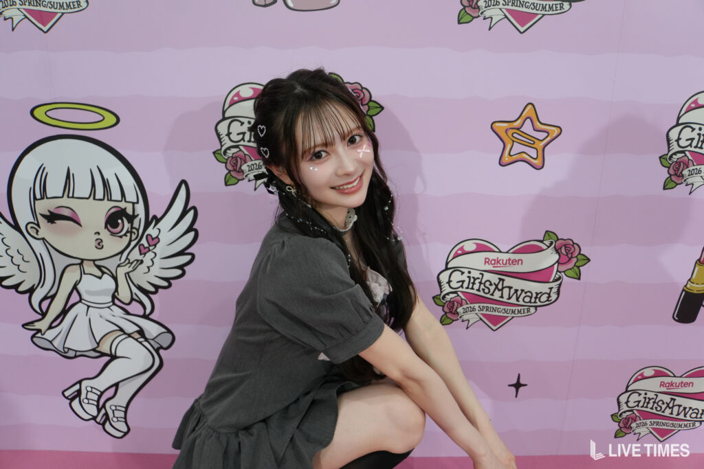 Young woman posing and smiling in front of a pink GirlsAward backdrop with graphics and logos.