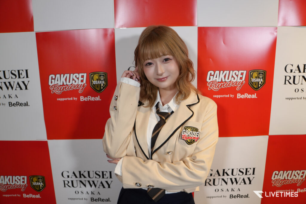 Young woman in a beige blazer posing in front of a red-and-white Gakusei Runway backdrop.