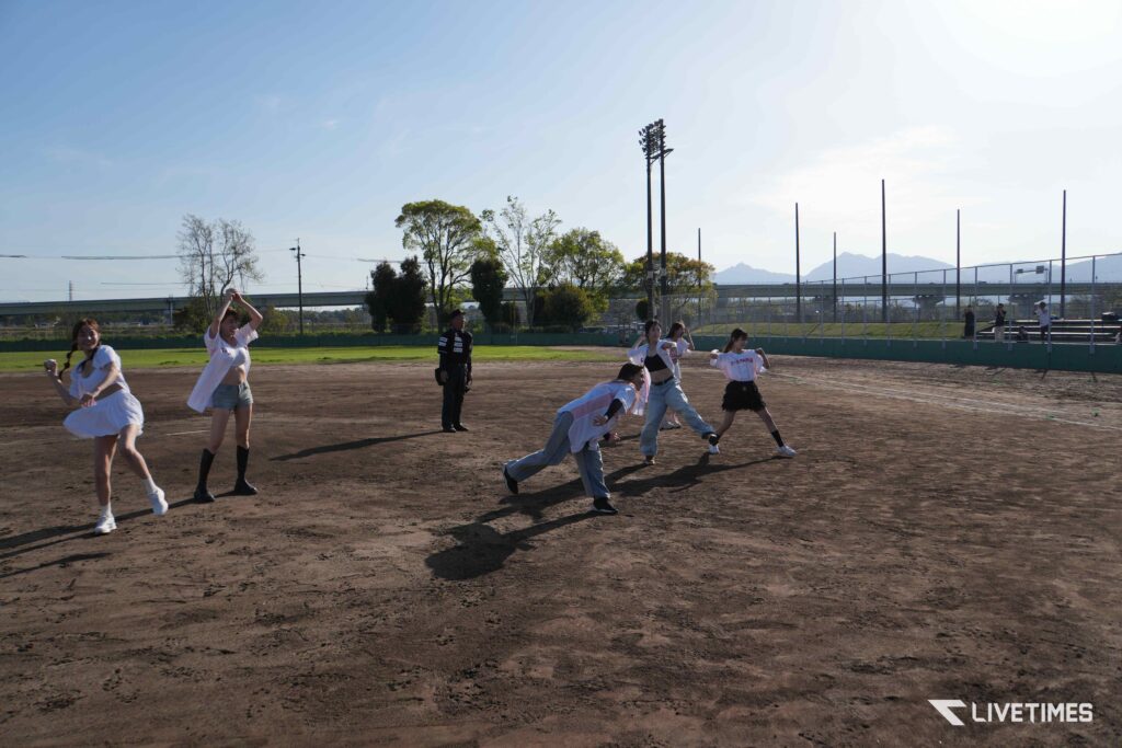 Group of players in white jerseys on a dusty baseball field, some running and throwing as a game unfolds under a clear sky