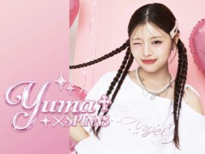 Portrait of a young woman with braids winking, wearing a white top, against a pink backdrop for Yuna × SPINNS promotional image.