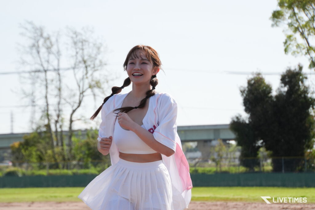 Young woman with two braids running outdoors on a sunny day, wearing a white athletic outfit with a pink cape.