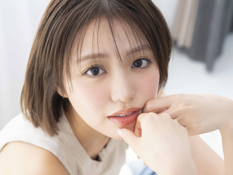 Close-up of a young woman with brown hair, looking to the side, hands near her mouth in a thoughtful pose.