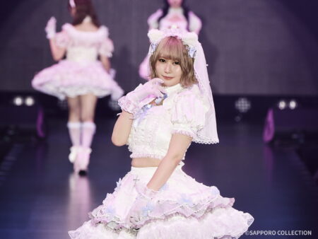 Young woman in a pink frilly stage costume with lace and bows, posing on a dark stage.