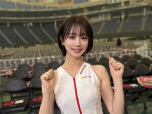 A woman in a white athletic outfit with a red zipper posing with fists up inside a stadium seating area, smiling at the camera.