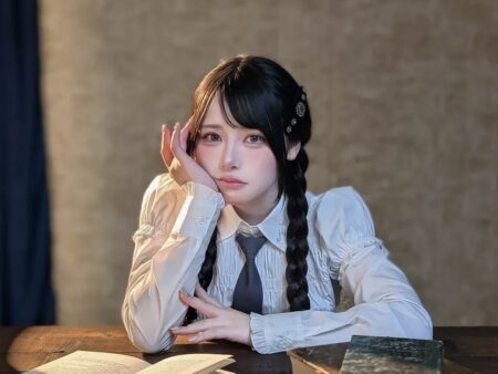 Young woman with long braids sits at a desk, resting her head on her hand in a contemplative pose.