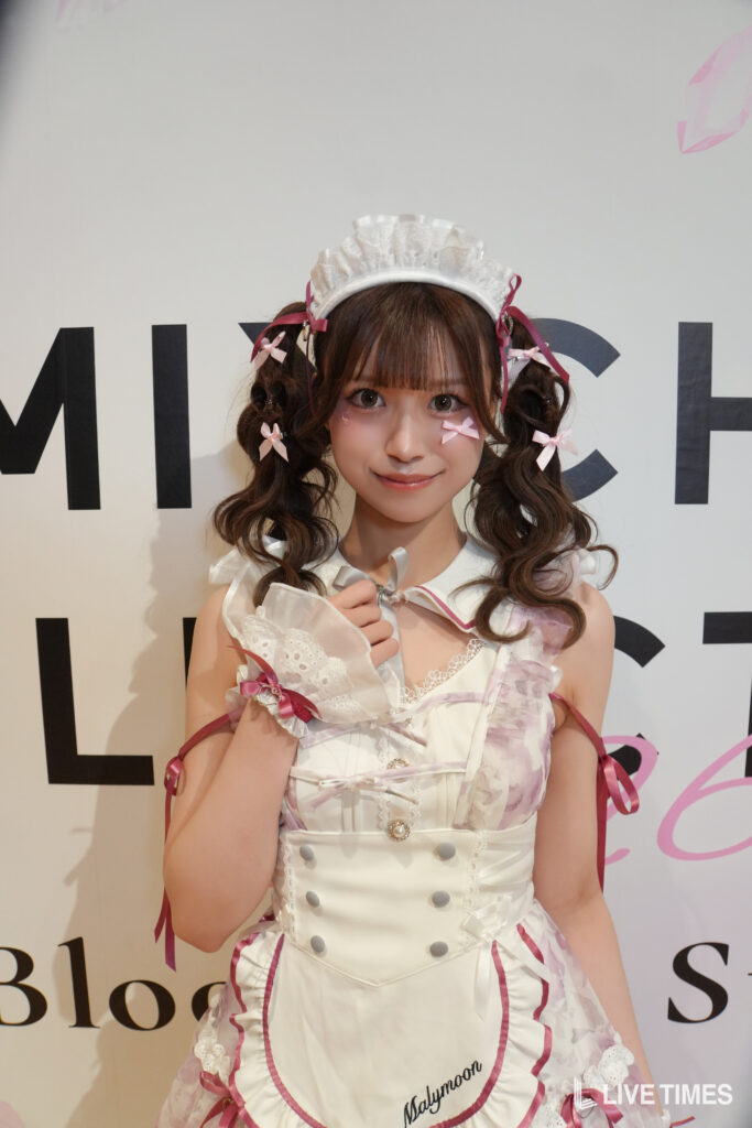 Young woman in a white and pink maid outfit with lace headband and curled pigtails posing for a photo defeat backdrop text behind her