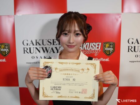 Smiling young woman holding a decorative certificate in front of a red-and-white backdrop with GAKUSEI RUNWAY OSAKA logos.