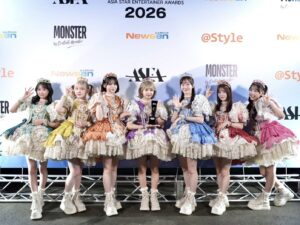Eight performers in colorful, ornate dresses with tiaras posing on a stage at the Asia Star Entertainer Awards 2026 image backdrop.