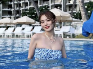 内田理央、ハワイオフショで水着&ツインテ姿披露 「綺麗すぎてAIかと思いました」と絶賛の声 Woman in a blue strapless swimsuit standing waist-deep in a resort pool, smiling at the camera with lounge chairs and umbrellas behind.