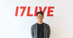 Man in a gray blazer stands before a white wall with a red 17LIVE logo behind him.