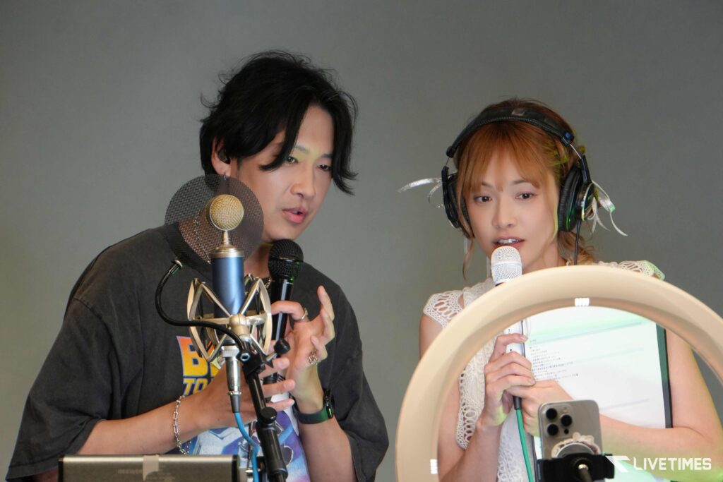 Two podcast hosts speaking into microphones in a studio, with a pop filter and headphones visible.