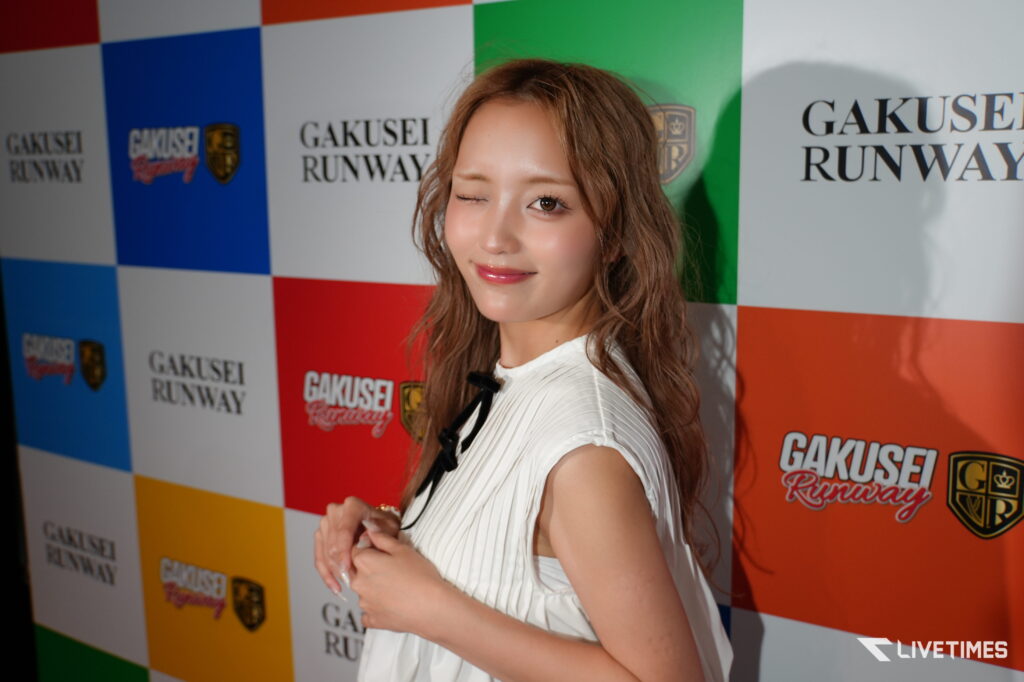 Young woman posing on a red carpet backdrop with 'GAKUSEI RUNWAY' logos and colorful checkered panels.