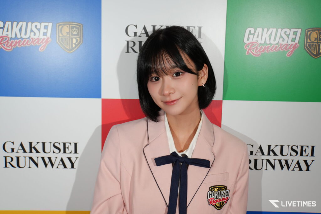 Young woman in a pale pink blazer with a navy bow, posing in front of a GAKUSEI RUNWAY backdrop.