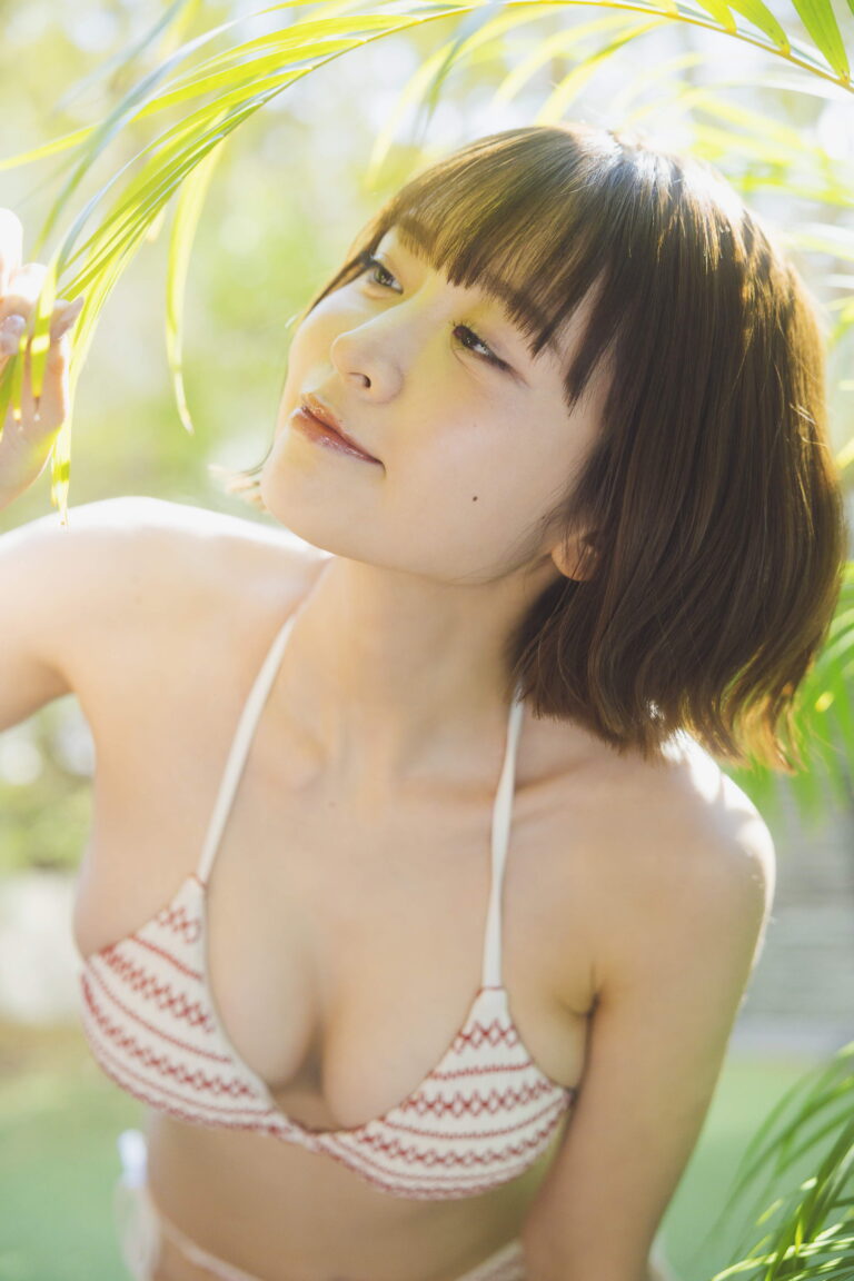 Young woman in a patterned bikini top leaning toward green palm leaves in bright outdoor sunlight.