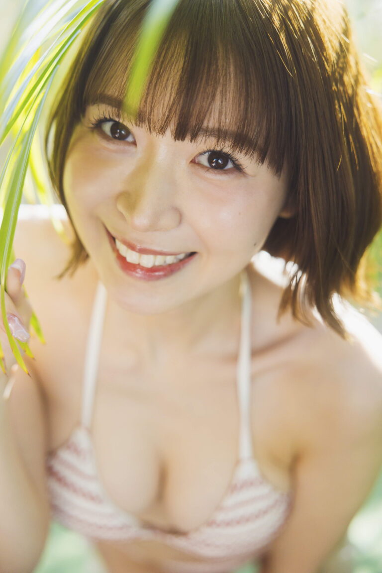 Close-up of a smiling young woman wearing a striped bikini top, with sunlight and green leaves in the background.