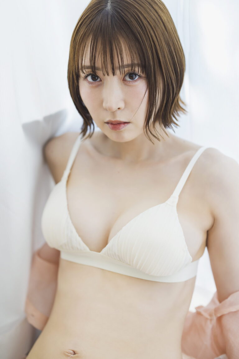 Close-up portrait of a young woman with short brown hair wearing a white bra, looking directly at the camera against a light background