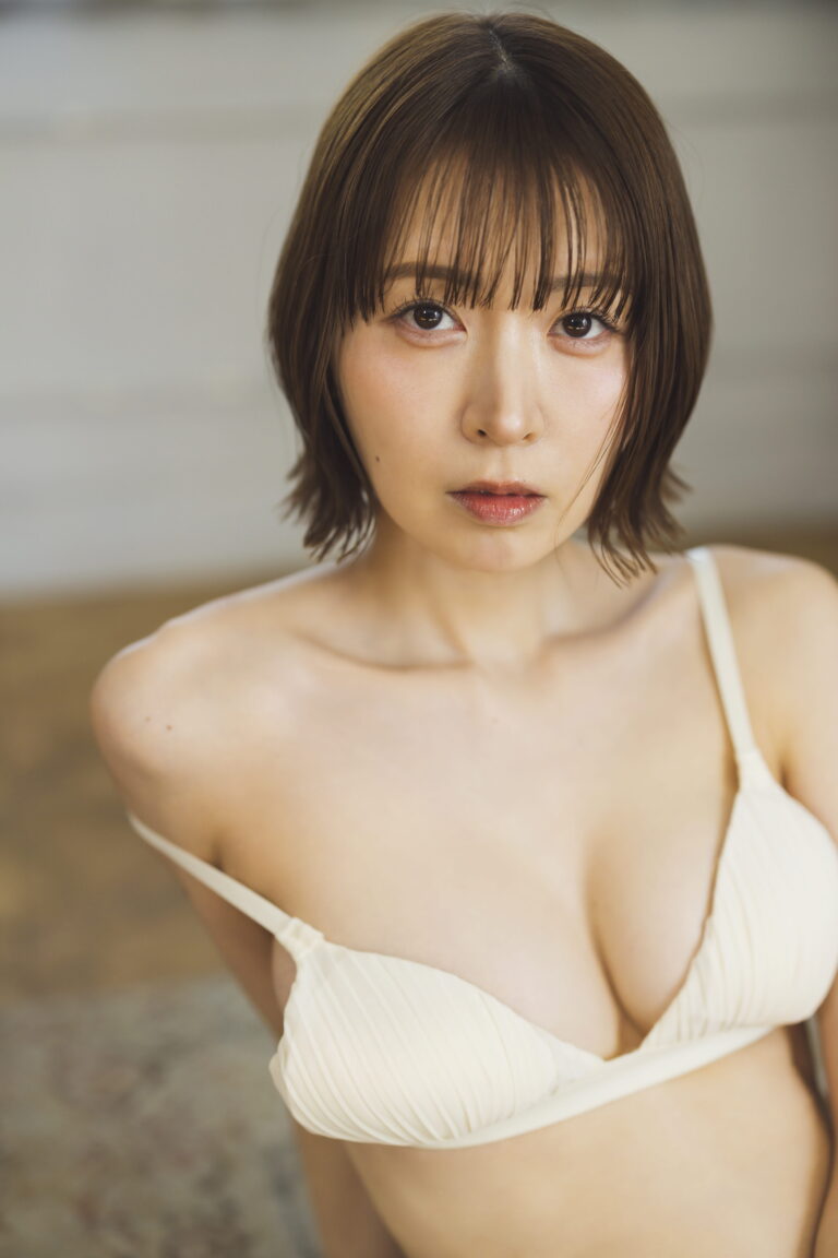 Close-up portrait of a young woman with short brown hair and bangs, wearing a cream ribbed bikini top and looking at the camera.