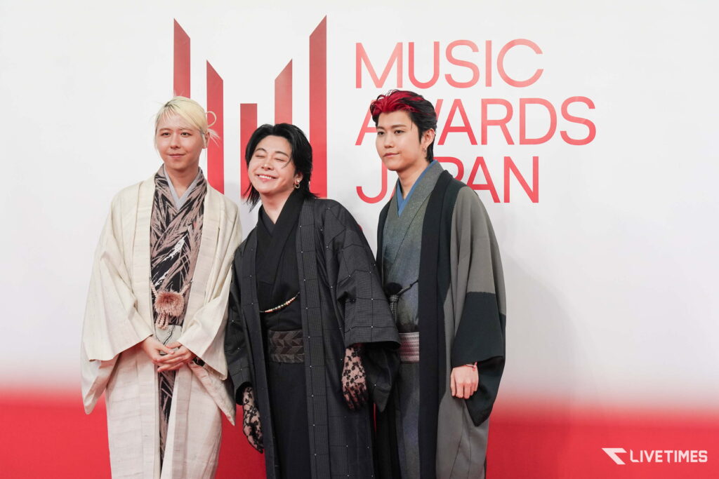 Three people in traditional robes posing on a red carpet at Music Awards Japan, Livetime logo bottom right.
