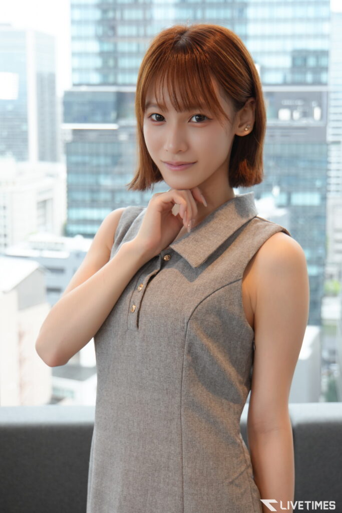 Portrait of a smiling woman with short brown hair in a gray sleeveless dress, with a city skyline behind her.