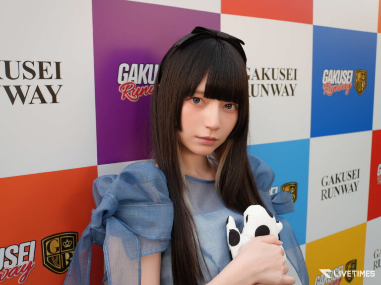 Young woman with long dark hair in a blue denim outfit posing against a colorful checkered backdrop with 'GAKUSEI RUNWAY' logos, holding a panda plush.