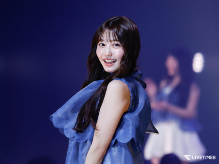 Smiling female performer in a blue dress on a stage with a purple backdrop.