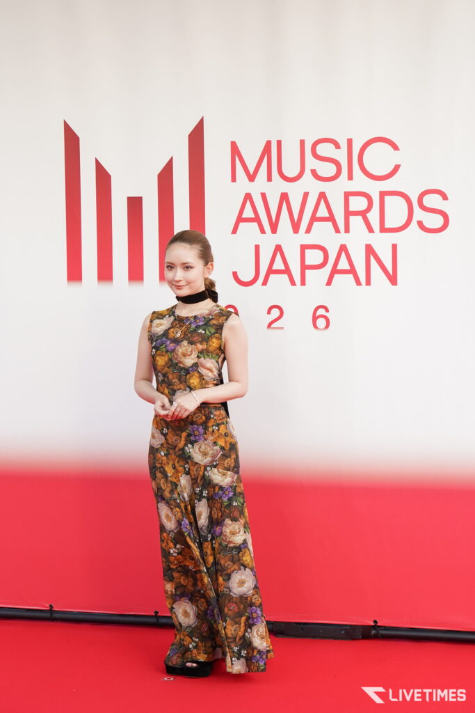 Female attendee posing on a red carpet in front of a Music Awards Japan 2016 backdrop with a red skyline graphic.