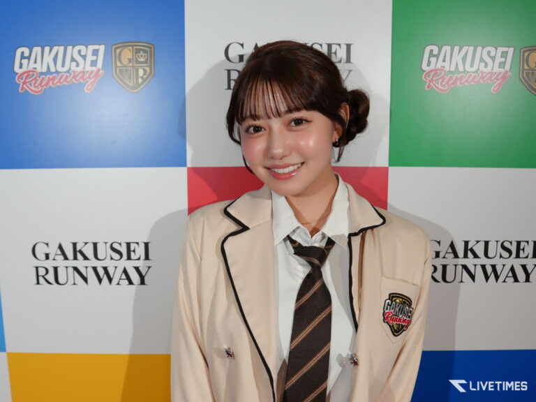 Smiling young woman in a beige blazer and striped tie posing in front of a blue/white/green backdrop with 'GAKU SEI RUNWAY' text.