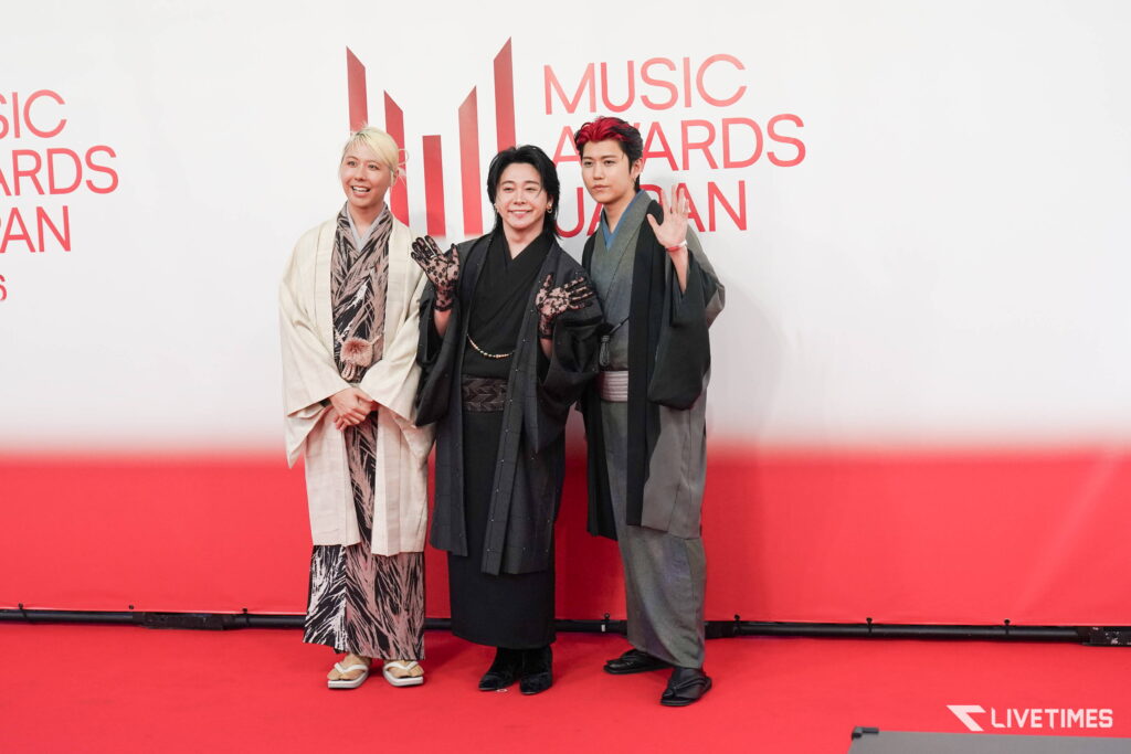 Three people in traditional Japanese kimonos posing on a red carpet at a Music Awards Japan event with a white backdrop.