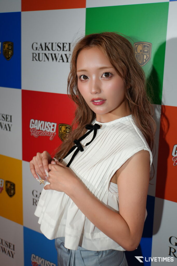 Young woman posing at a fashion event in front of a colorful checkered backdrop with GAKUSEI RUNWAY logos.