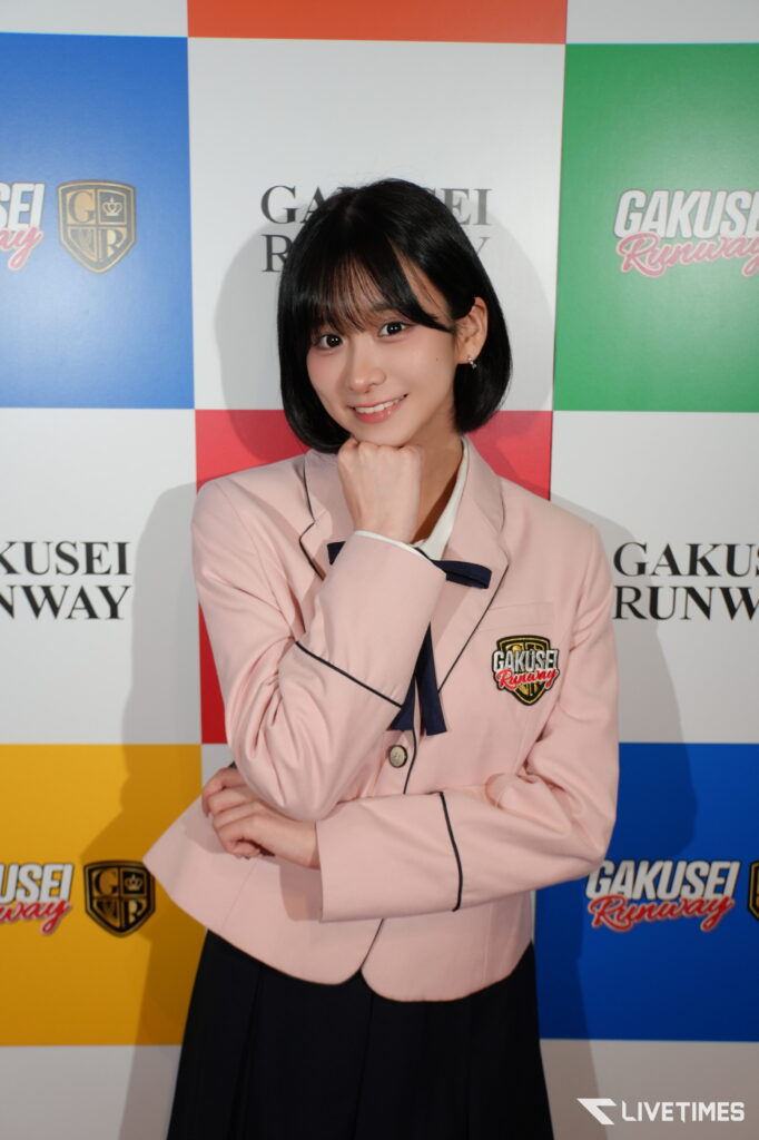 Young woman with short black hair in a pale pink blazer, posing with chin on her hand in front of a colorful backdrop reading GAKUSEI RUNWAY.