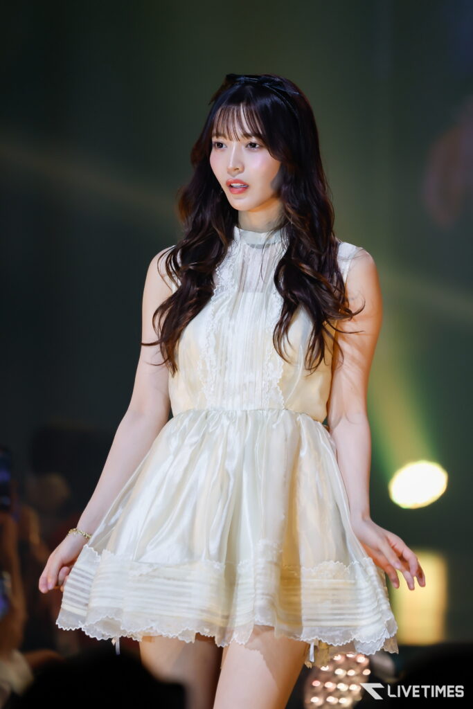 Young woman in a cream lace dress performing on stage, with soft spotlight on her face.