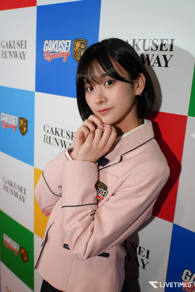 Young woman with short black hair posing in a pink blazer in front of a colorful GAKUSEI RUNWAY backdrop.