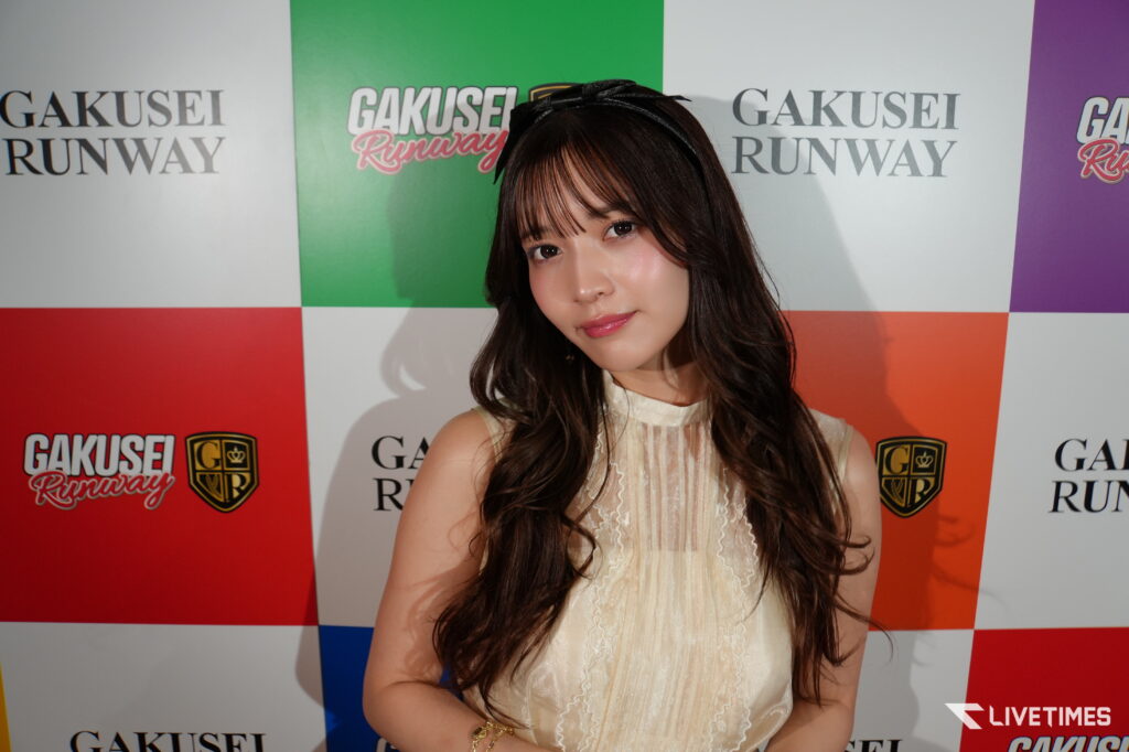 Young woman poses for a photo at a fashion event, standing in front of a colorful backdrop with Gakusei Runway logos and branding.