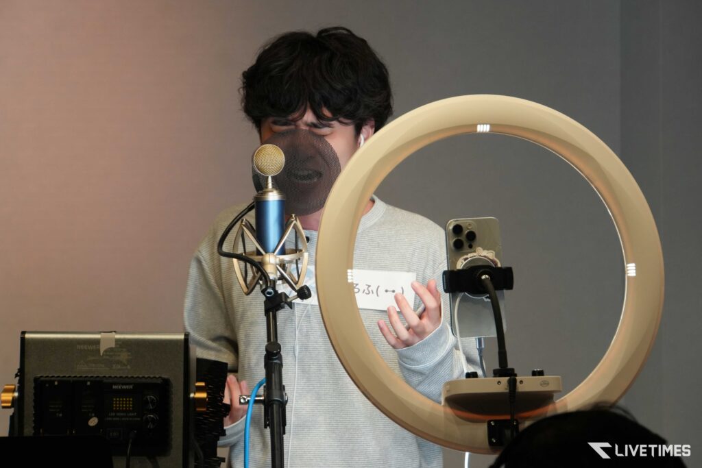 Person recording vocals in a studio, speaking into a microphone with a pop filter and ring light nearby.