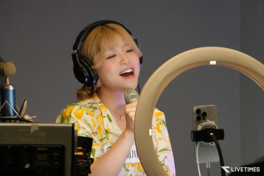 Young woman wearing over-ear headphones sings into a mic in a recording studio with a pop filter nearby