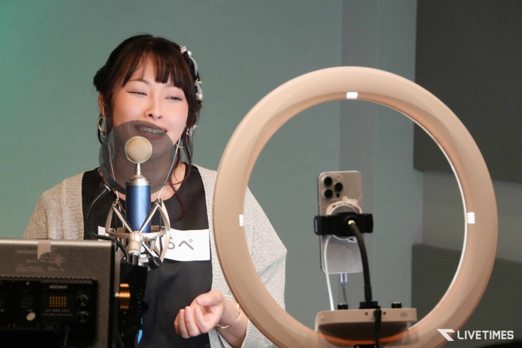 Woman singing into a microphone with a pop filter in a recording studio, ring light visible beside her