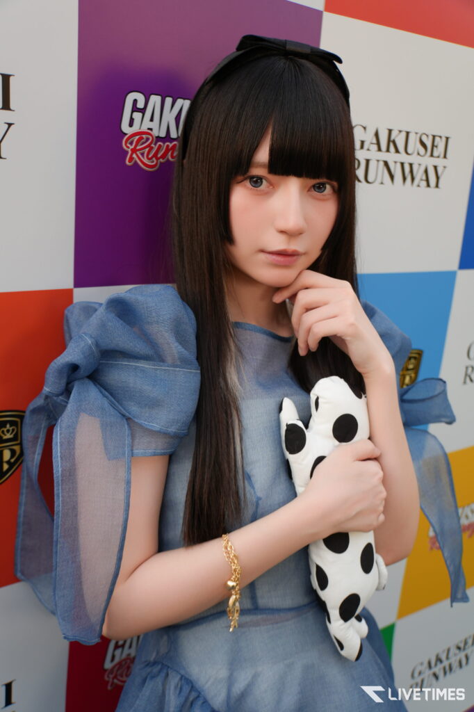 Young woman with long black hair in a blue dress holds a panda-patterned stuffed toy, posing in front of a colorful backdrop.
