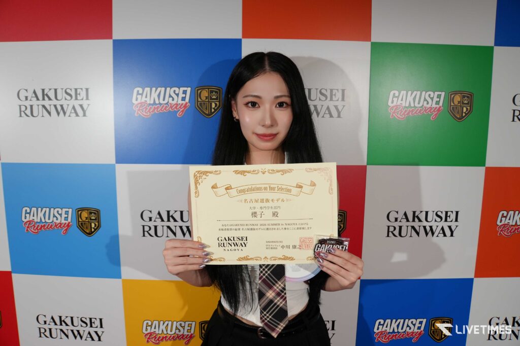 Young woman posing with a large certificate in front of a colorful GAKUSEI RUNWAY backdrop.