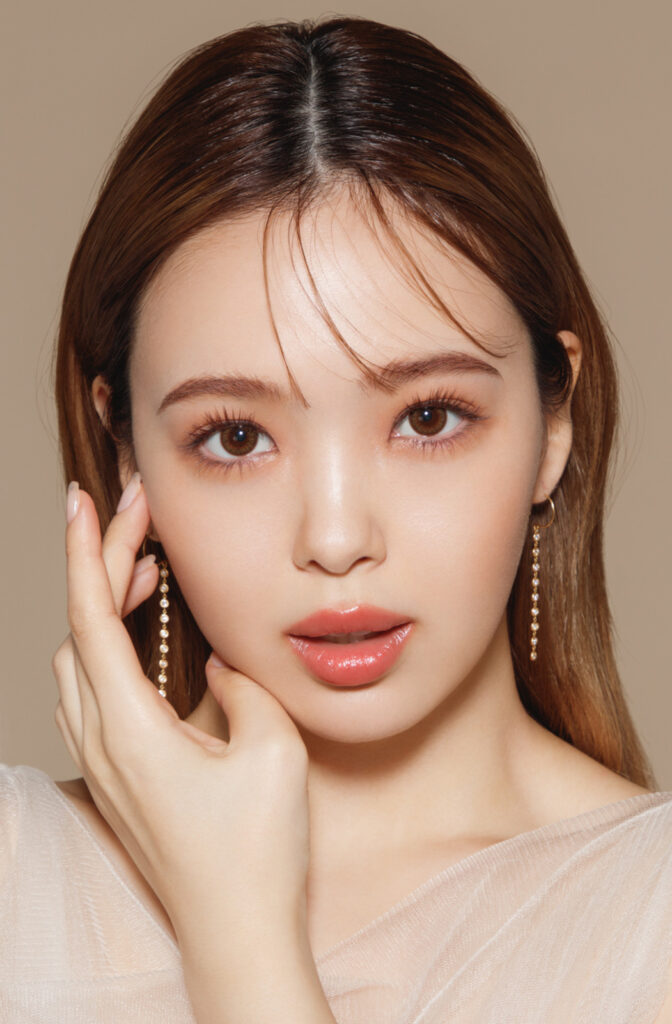 Close-up portrait of a woman with brown hair and pearl drop earrings, touching her cheek.