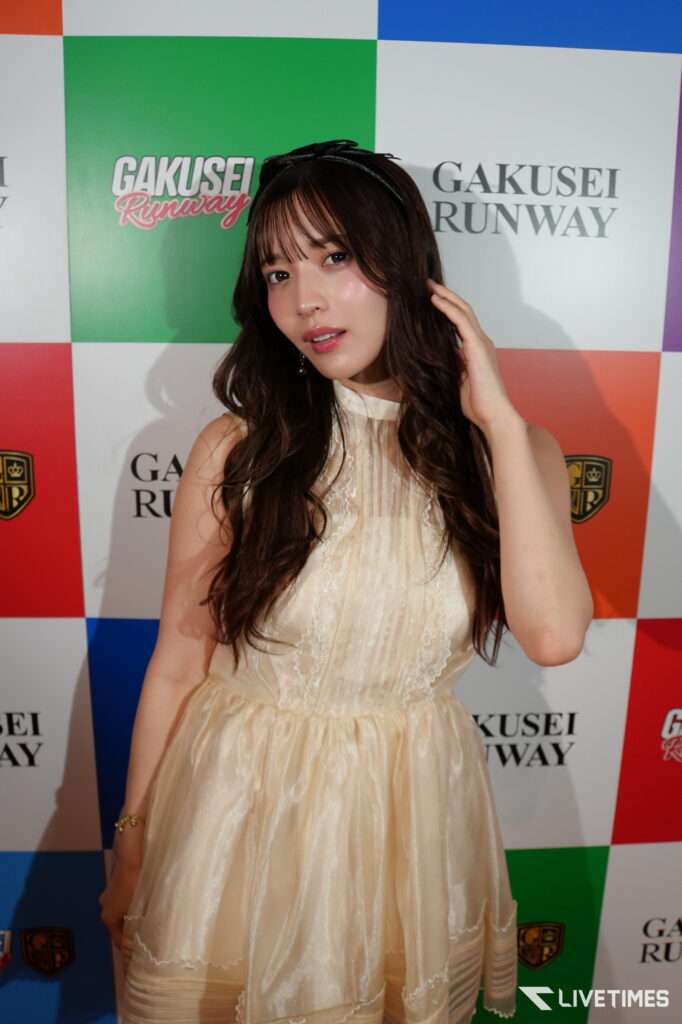 Young woman in a cream lace dress posing on a colorful backdrop with 'GAKUSEI RUNWAY' branding.