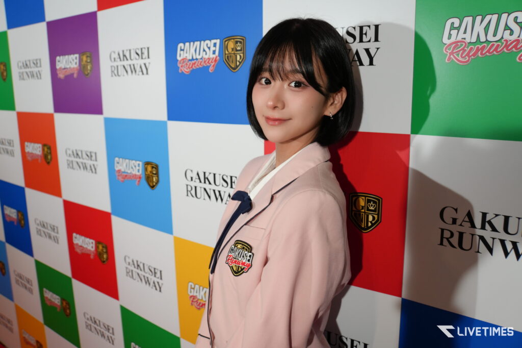 Young woman posing in front of a colorful checkered backdrop with GAKUSEI RUNWAY logos at a fashion event.